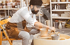 A young male potter is engaged in craft in his workshop on a potter`s wheel and makes a clay product