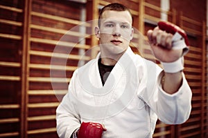 Young male practicing judo in kimono with fight glove.