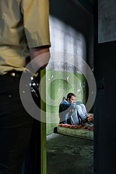 Young male prisoner sitting alone in an obsolete prison cell