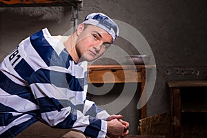 Young male prisoner wearing prison uniform looks at the camera w