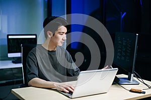 Young male programmer working with tablet and screen displaying code. Modern tech office setup, great for software, coding, IT