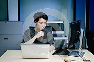 Young male programmer working with tablet and screen displaying code. Modern tech office setup, great for software, coding, IT