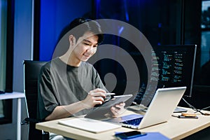 Young male programmer working with tablet and screen displaying code. Modern tech office setup, great for software, coding, IT