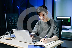 Young male programmer working with tablet and screen displaying code. Modern tech office setup, great for software, coding, IT