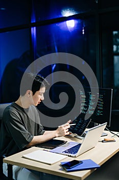 Young male programmer working with tablet and screen displaying code. Modern tech office setup, great for software, coding, IT