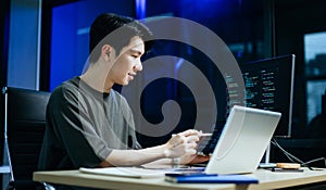 Young male programmer working with tablet and screen displaying code. Modern tech office setup, great for software, coding, IT