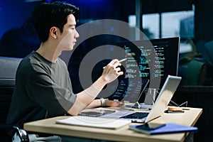 Young male programmer working with tablet and screen displaying code. Modern tech office setup, great for software, coding, IT