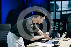 Young male programmer working with tablet and screen displaying code. Modern tech office setup, great for software, coding, IT