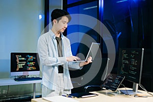 Young male programmer working with tablet and screen displaying code. Modern tech office setup, great for software
