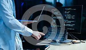 Young male programmer working with tablet and screen displaying code. Modern tech office setup, great for software