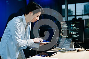 Young male programmer working with tablet and screen displaying code. Modern tech office setup, great for software