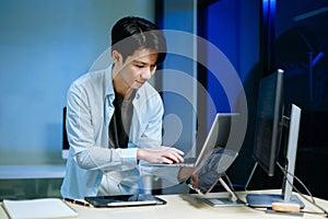 Young male programmer working with tablet and screen displaying code. Modern tech office setup, great for software