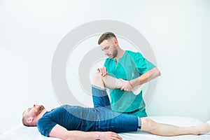 Young male receiving massage from therapist. A chiropractor stretching his patient`s legs in medical office. Neurological physica