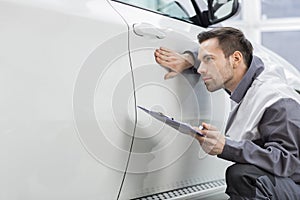 Young male repair worker examining car in automobile repair shop