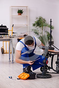 Young male repairer repairing perambulator indoors