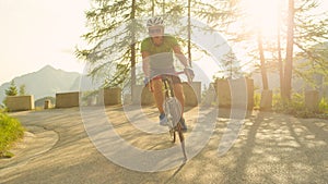 Young male road cyclist having fun pedalling up steep asphalt road on sunny day