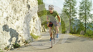 Young male road cyclist pedalling up a steep mountain road on sunny summer day.