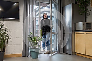 Young male robber in dark clothes carefully and quietly enters through the balcony window into the apartment, house. Holds scrap