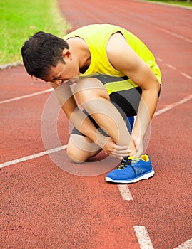 Young male runner with ankle injury on track