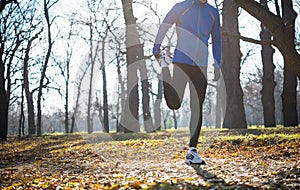 Young Male Runner Stretching in the Park in Cold Sunny Autumn Morning. Healthy Lifestyle and Sport Concept.