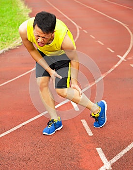 Young male runner suffering from leg cramp on the track