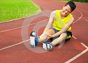 Young male runner suffering from leg cramp on the track