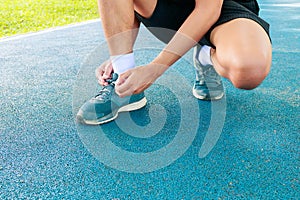 Young male runner tying shoelaces old in runner exercise for health lose weight concept on track rubber cover blue public park