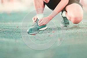 Young male runner tying shoelaces old in runner exercise for health lose weight concept on track rubber cover blue public park