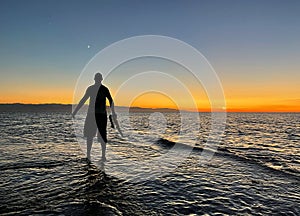 Young male saxophonist stands with his feet in sea water, holds saxophone in his hands, looks at sunset. Beautiful sunset on sea,