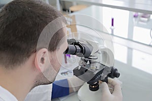 Young male male scientist looking through a microscope in a labo photo