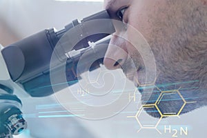 Young male male scientist looking through a microscope in a labo photo