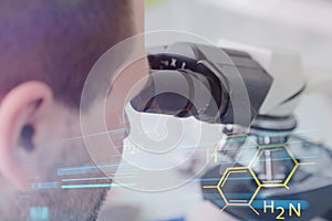 Young male male scientist looking through a microscope in a labo photo