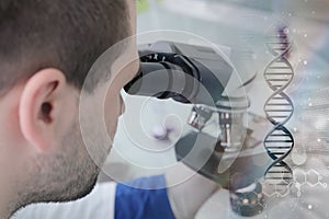 Young male male scientist looking through a microscope in a labo photo