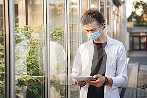 Young male scientist monitoring plant development with digital tablet in glasshouse during COVID-19 outbreak