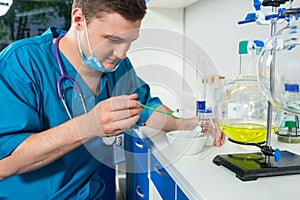 Young male scientist in uniform wearing a mask preparing powder