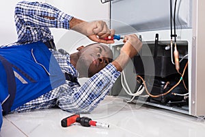 Male Serviceman Working On Fridge With Screwdriver photo