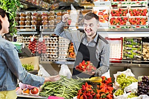 Young male shopping assistant helping customer to buy fruit and