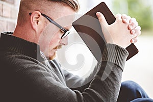 Young male sitting on the ground and holding the bible in his hands