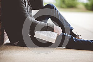 Young male sitting on the ground and holding the bible in his hands