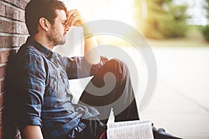 Young male sitting on the ground and holding the bible in his hands-thoughtful, mindful concepts