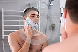 Young male smearing foam for shave on his face