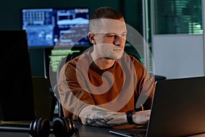 Young Male Software Developer Coding on Laptop while Sitting at Working Desk in Office