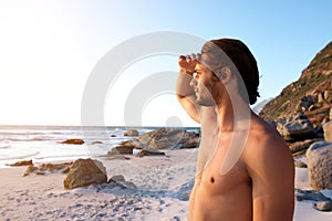 Young male standing at beach looking at water