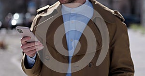 Young male standing on the city street using mobile phone app. Man using smartphone, typing message, browsing internet