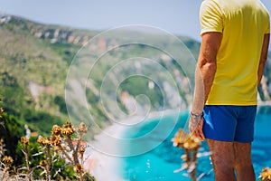 Young male staying in front of Petani beach on Kefalonia. Highly excited picturesque panorama of emerald blue lagoon bay