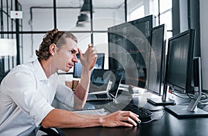 Young male stock brocker works indoors in the office. Many of displays photo