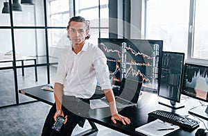 Young male stock brocker works indoors in the office. Many of displays