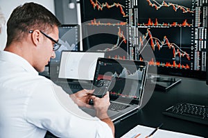 Young male stock brocker works indoors in the office. Many of displays