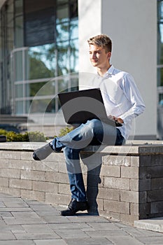 Young male student or bloger using laptop on the street.