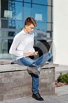 Young male student or bloger using laptop on the street.